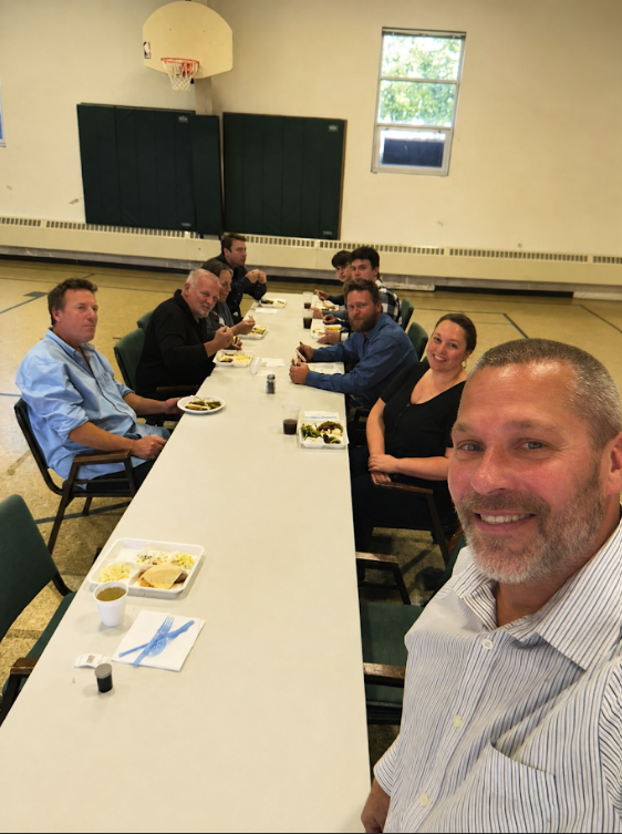Neighbors seated around a long table sharing a community meal in the church hall